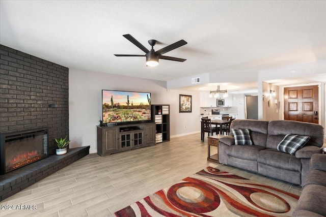 living room featuring visible vents, ceiling fan, a brick fireplace, baseboards, and light wood-type flooring