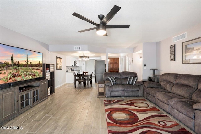 living room featuring visible vents, light wood-type flooring, and ceiling fan with notable chandelier