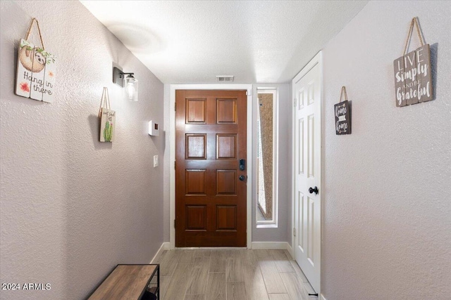 foyer featuring baseboards, light wood-style floors, and a textured wall
