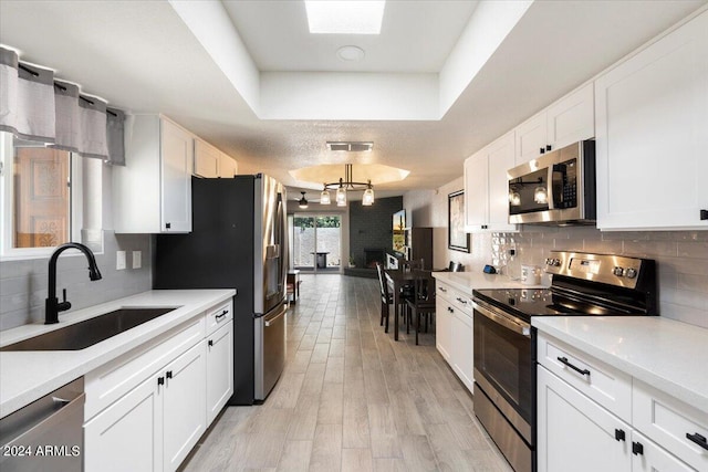 kitchen featuring white cabinetry, a sink, stainless steel appliances, a tray ceiling, and backsplash