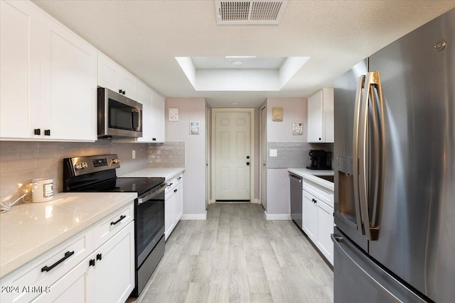 kitchen featuring stainless steel appliances, light countertops, white cabinets, visible vents, and a raised ceiling