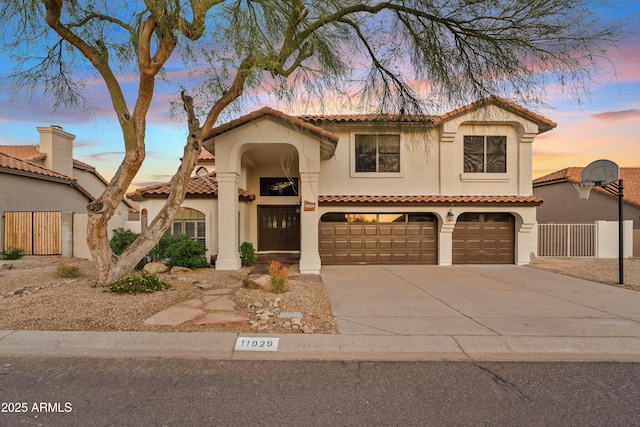 mediterranean / spanish-style house with stucco siding, driveway, an attached garage, and fence