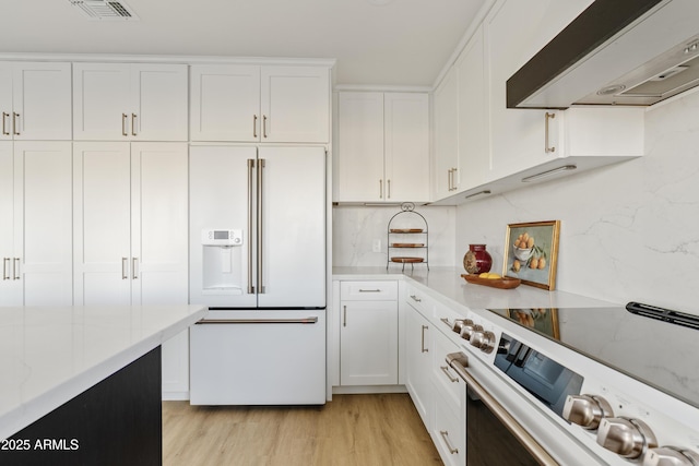 kitchen with visible vents, high end white refrigerator, white cabinetry, wall chimney range hood, and range