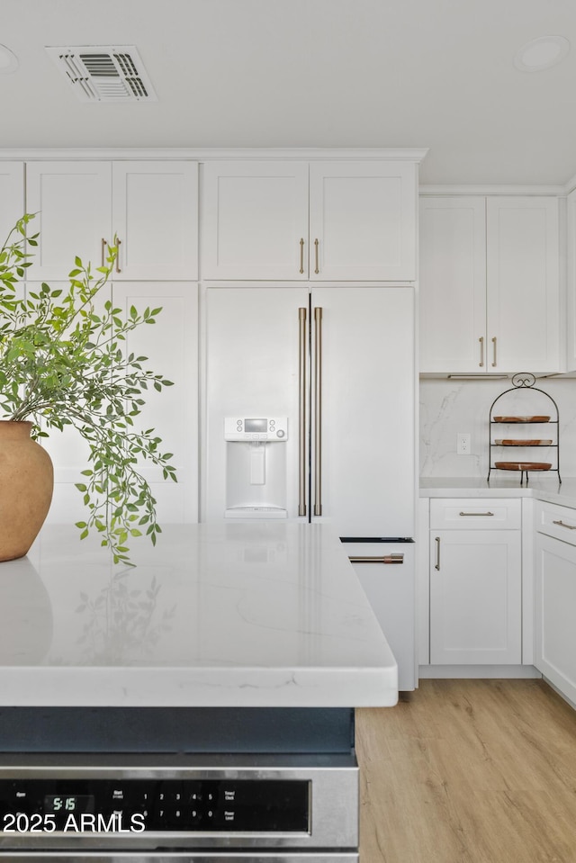 kitchen with light stone counters, visible vents, light wood-style flooring, high end fridge, and white cabinetry