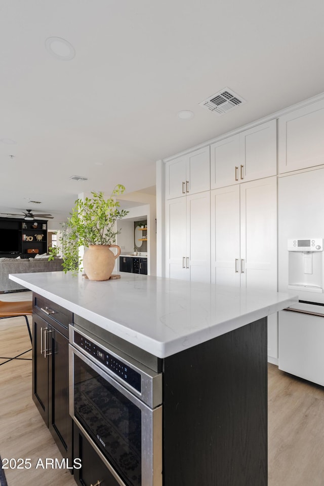 kitchen with light wood finished floors, visible vents, a center island, light stone countertops, and white cabinetry