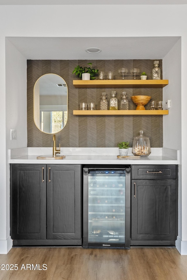 bar featuring wood finished floors, a dry bar, beverage cooler, and a sink