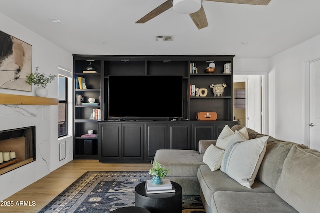 living area with visible vents, ceiling fan, a high end fireplace, and light wood finished floors