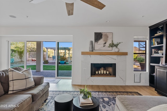 living area with a premium fireplace, a healthy amount of sunlight, wood finished floors, and a ceiling fan