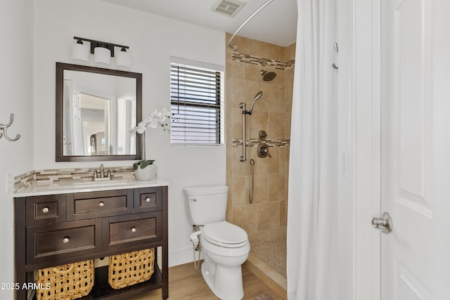 full bath with vanity, wood finished floors, visible vents, a tile shower, and toilet