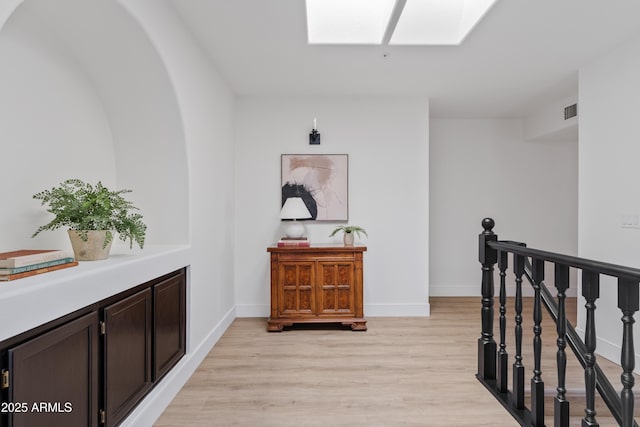 corridor with visible vents, an upstairs landing, light wood-style floors, a skylight, and baseboards