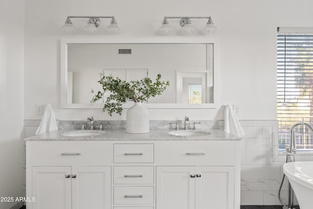 full bath featuring a sink, visible vents, double vanity, and a freestanding tub