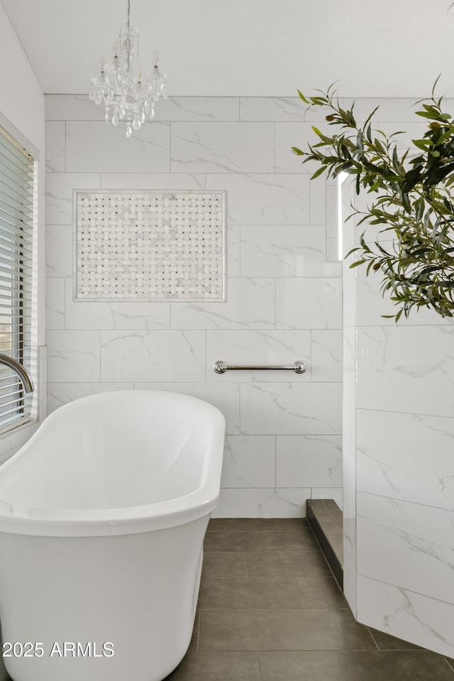 full bathroom featuring tile walls, an inviting chandelier, and a freestanding tub