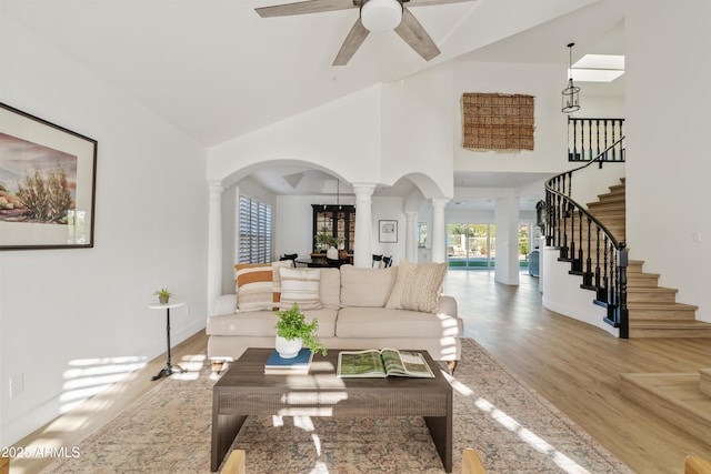 living room with stairway, wood finished floors, a ceiling fan, ornate columns, and arched walkways