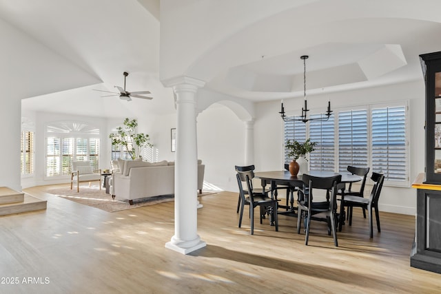 dining space featuring a tray ceiling, decorative columns, light wood-type flooring, and ceiling fan with notable chandelier