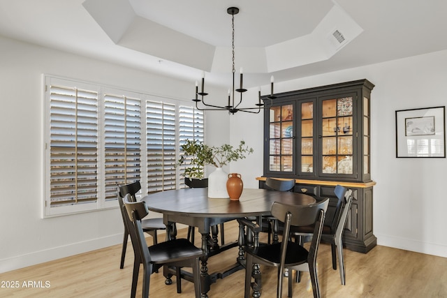 dining space featuring light wood-type flooring, a tray ceiling, baseboards, and an inviting chandelier