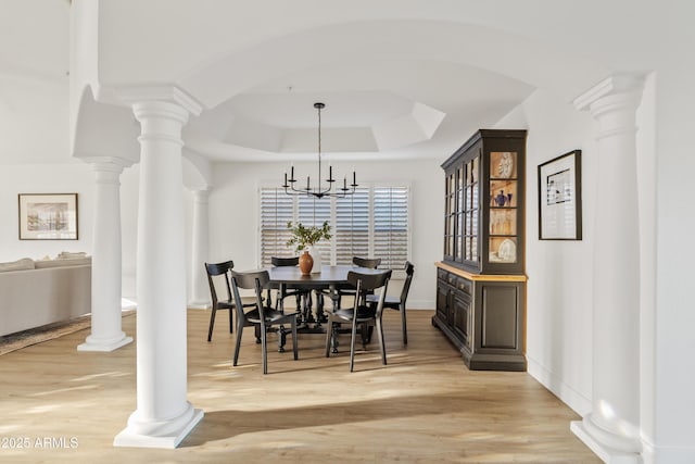 dining space featuring a tray ceiling, a notable chandelier, light wood-type flooring, and ornate columns