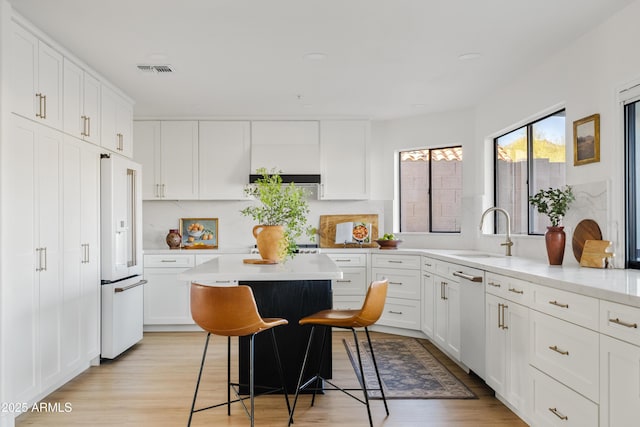 kitchen with high end white refrigerator, white cabinets, visible vents, and a sink