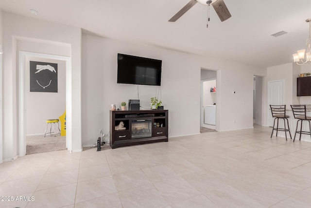 tiled living room with ceiling fan with notable chandelier and washer / dryer