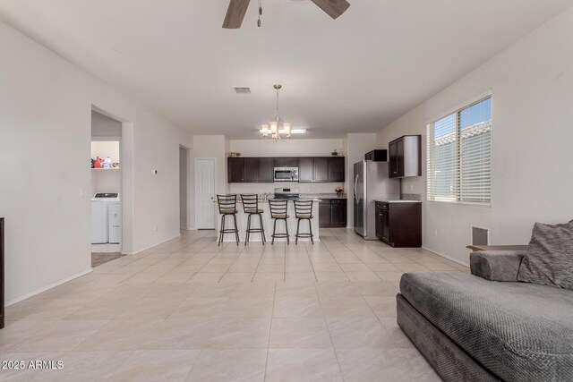 tiled living room with washer / dryer and ceiling fan with notable chandelier