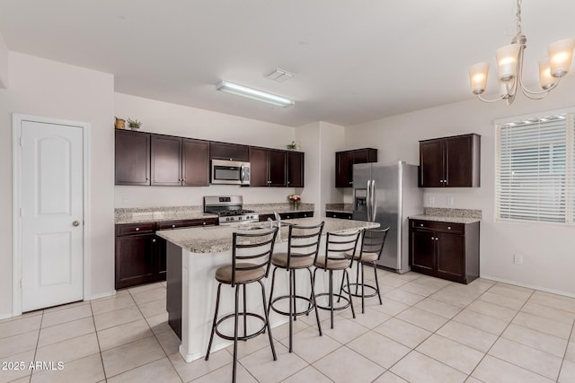 kitchen with stainless steel appliances, an island with sink, dark brown cabinetry, an inviting chandelier, and decorative light fixtures