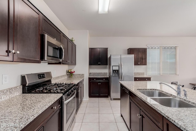 kitchen featuring appliances with stainless steel finishes, light tile patterned floors, light stone counters, sink, and dark brown cabinets