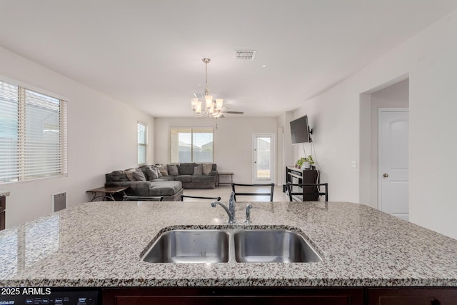 kitchen featuring sink, a kitchen island with sink, dark brown cabinets, and light stone counters