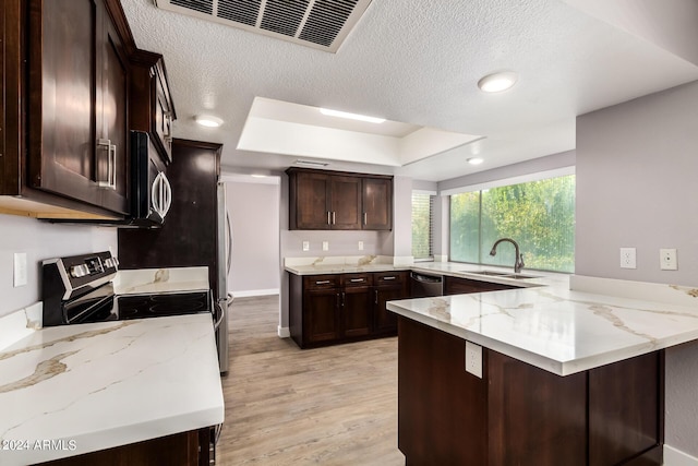 kitchen featuring sink, light wood-type flooring, appliances with stainless steel finishes, kitchen peninsula, and light stone countertops