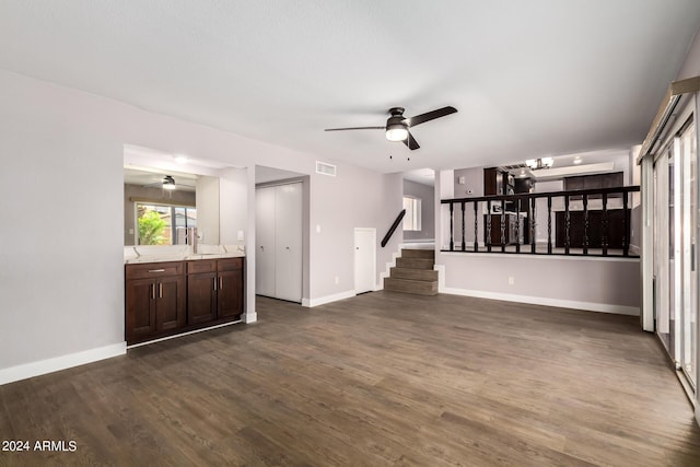 unfurnished living room with dark wood-type flooring, visible vents, stairway, and a ceiling fan