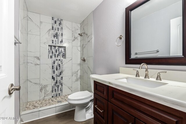 bathroom featuring vanity, wood-type flooring, toilet, and tiled shower