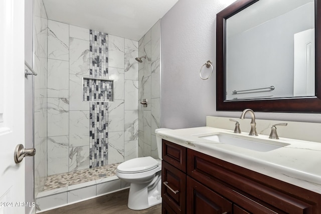 bathroom with a textured wall, toilet, wood finished floors, vanity, and a stall shower