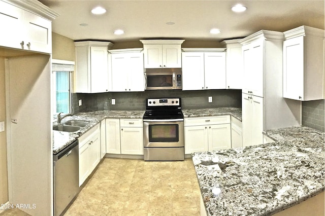 kitchen with light stone counters, a sink, white cabinets, appliances with stainless steel finishes, and tasteful backsplash