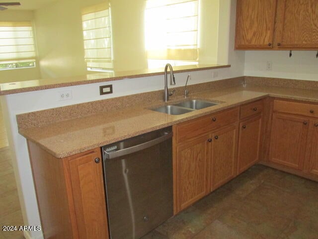 kitchen featuring stainless steel dishwasher, light stone counters, sink, and dark tile patterned floors