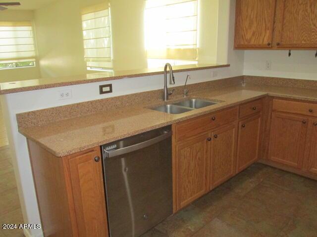 kitchen with light stone countertops, a sink, stainless steel dishwasher, and a peninsula