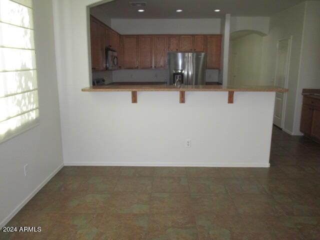 kitchen with a kitchen breakfast bar, a peninsula, brown cabinetry, stainless steel refrigerator with ice dispenser, and arched walkways