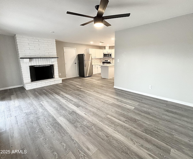 unfurnished living room with ceiling fan, a brick fireplace, and light wood-type flooring