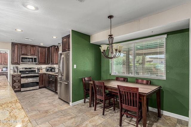 8620 E Sells Dr, Scottsdale, AZ 85251 - kitchen with stainless steel appliances, dark brown cabinetry, a chandelier, light stone finish flooring, and recessed lighting