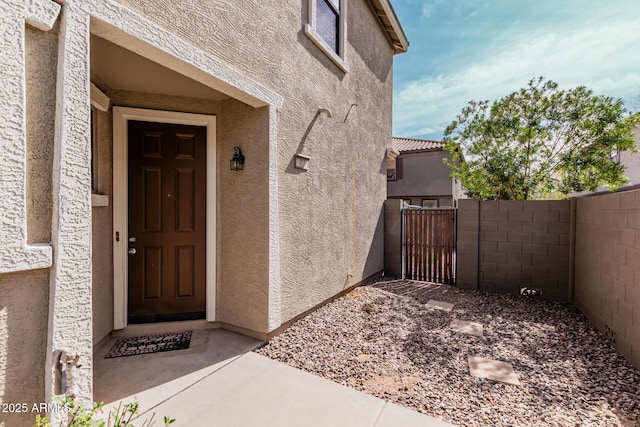 view of exterior entry featuring a tile roof, a gate, fence, and stucco siding