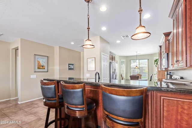 kitchen with kitchen peninsula, stainless steel appliances, a breakfast bar, light tile patterned flooring, and pendant lighting