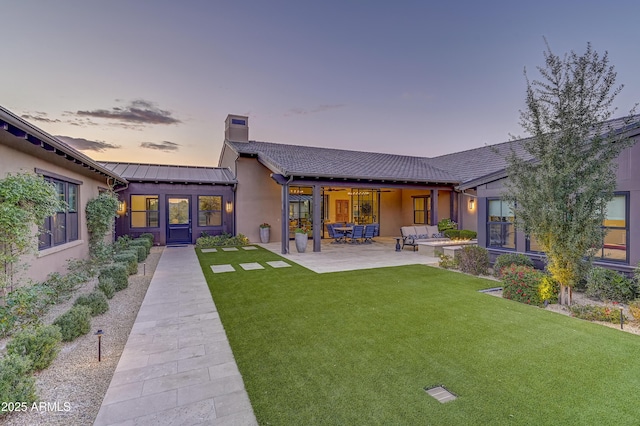 back house at dusk with a lawn, a patio area, and an outdoor hangout area