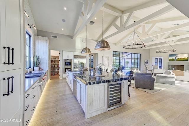 kitchen featuring beam ceiling, white cabinetry, beverage cooler, a spacious island, and decorative light fixtures