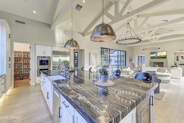 kitchen featuring pendant lighting, high vaulted ceiling, dark stone counters, white cabinetry, and stainless steel appliances