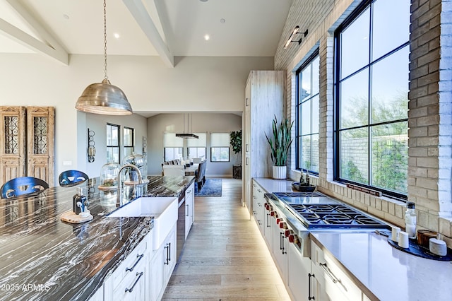 kitchen with pendant lighting, stainless steel gas stovetop, white cabinets, sink, and light hardwood / wood-style flooring