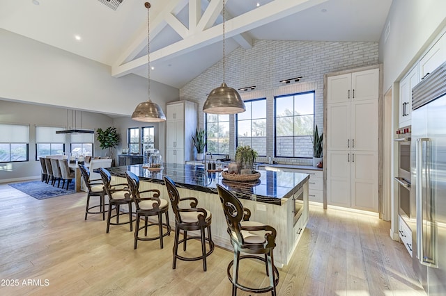 kitchen with beam ceiling, white cabinetry, a large island, hanging light fixtures, and a breakfast bar