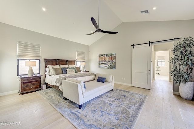 bedroom with ceiling fan, a barn door, light wood-type flooring, and high vaulted ceiling