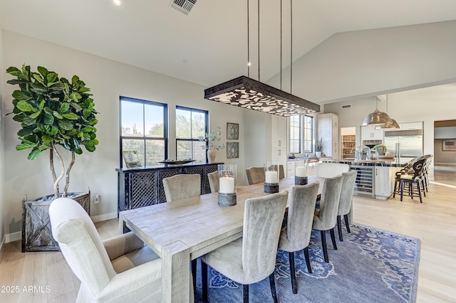 dining area featuring light hardwood / wood-style flooring, vaulted ceiling, beverage cooler, and a healthy amount of sunlight