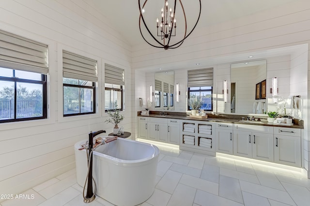 bathroom with tile patterned floors, vanity, vaulted ceiling, an inviting chandelier, and a tub