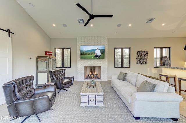 living room with a barn door, a brick fireplace, and ceiling fan