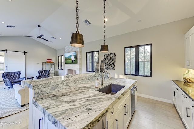 kitchen with light stone countertops, sink, hanging light fixtures, a center island with sink, and white cabinets