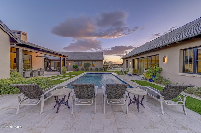 pool at dusk featuring pool water feature and a patio area