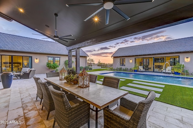 pool at dusk featuring an outdoor living space, pool water feature, ceiling fan, and a patio area